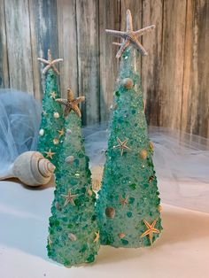 two small christmas trees made out of sea glass with starfish on top and seashells in the background