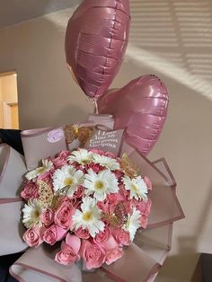 a bouquet of pink roses and white daisies in a gift box with balloons attached