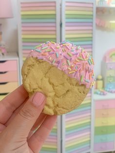 a hand holding a doughnut with pink frosting and sprinkles