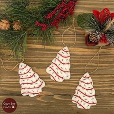 three christmas ornaments hanging from string on wooden table next to pine cones and red berries