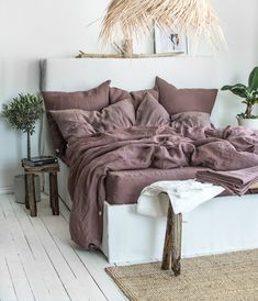 an unmade bed with pillows and blankets on it in a room next to a potted plant