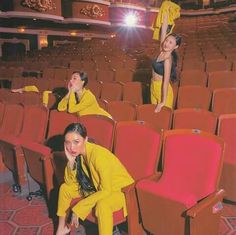 two women in yellow outfits are sitting on red chairs and one woman is standing behind them