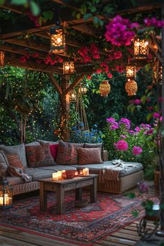 an outdoor living area is lit up with candles and flowers on the table, surrounded by greenery