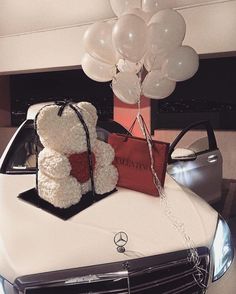 a teddy bear sitting on the hood of a car with balloons in the shape of hearts