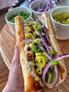 a hand holding a sandwich with onions, peppers and other condiments on the side