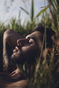 a man laying in the grass with his eyes closed and head tilted to the side