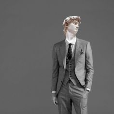 a man wearing a suit and tie standing in front of a gray background