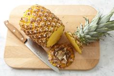 a pineapple cut in half on a cutting board with a knife