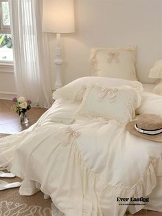 a white bed in a bedroom next to a window with curtains and pillows on it