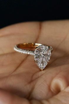 a woman's hand holding an engagement ring with a pear shaped diamond on it