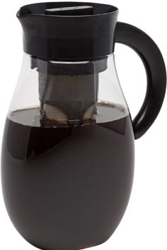 a glass pitcher filled with liquid on top of a white table next to a black lid