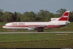 a red and white plane is on the runway at an airport with trees in the background