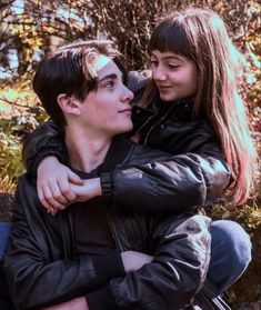 a young man and woman hugging each other in front of some trees with leaves on them