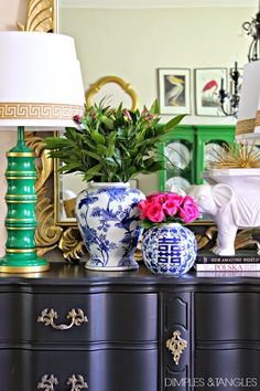 a blue dresser with two lamps on top of it next to a mirror and vases