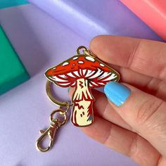 a hand holding a red and white mushroom shaped keychain with blue nail polish