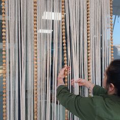 a woman is working on some beads hanging in front of a window with her hands