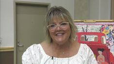 a woman wearing glasses standing in front of a wall with an art work on it