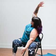 a woman with purple hair sitting in a chair on a yoga mat and stretching her arms