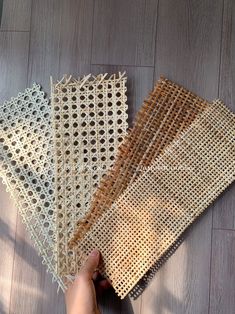 four pieces of woven fabric laid out on a wooden floor with one person's hand