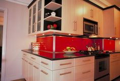 a kitchen with white cabinets and red backsplashing on the counter top,