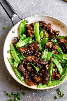 a bowl filled with meat and green beans on top of a gray surface next to chopsticks