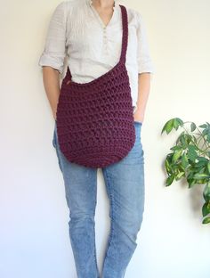 a woman is holding a crocheted bag in her hands while standing next to a potted plant