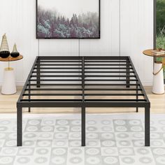 a metal bed frame in a white room with wood flooring and artwork on the wall