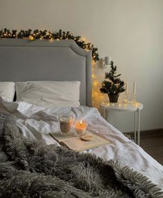 a bed with two candles on top of it next to a night stand and christmas lights