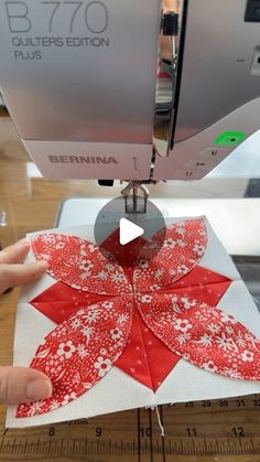 someone is using a sewing machine to sew a red and white flower ornament