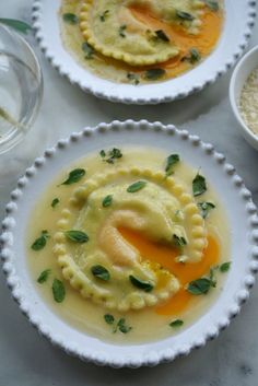 three white plates topped with ravioli and sauces on top of a marble table