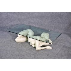 a glass table that has a statue on it with a person laying down in front of it