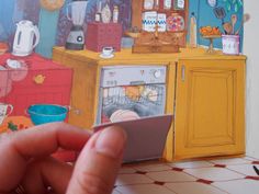 a hand holding an object in front of a drawing of a kitchen with ovens and cabinets