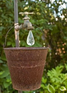 an old fashioned water faucet hanging from a metal pole in front of trees