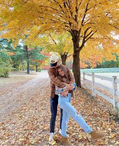 a man and woman are hugging in the fall leaves near a tree with yellow leaves on it