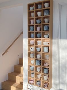 a wooden shelf filled with lots of cups on top of a hard wood floor next to a stair case