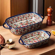 two serving dishes on a counter with utensils and orange slices next to them