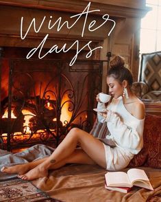 a woman sitting in front of a fireplace holding a cup of coffee and reading a book