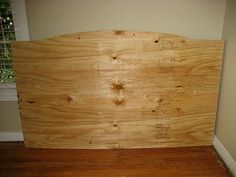 a wooden headboard sitting on top of a hard wood floor next to a window