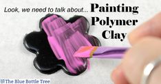 a hand holding a paintbrush painting a polymer clay flower with pink and black colors