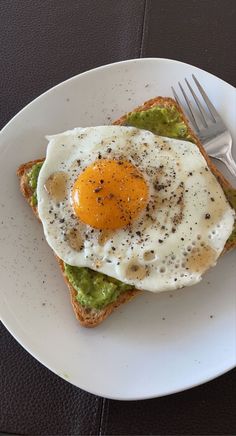 an egg and avocado toast on a white plate with a fork next to it