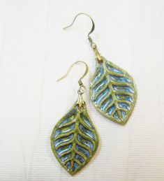 two green and blue leaf shaped earrings on a white surface with gold earwires