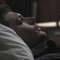 a man laying in bed with his eyes closed and head turned to the side, looking off into the distance