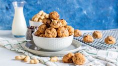 a white bowl filled with cookies next to a glass of milk and some peanuts on a plate