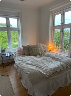 a white bed sitting in a bedroom next to two windows with lots of light on them