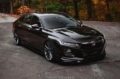 a black car parked in a parking lot next to some trees with leaves on them