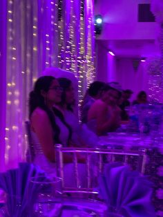 two women standing next to each other in front of purple lights at a wedding reception