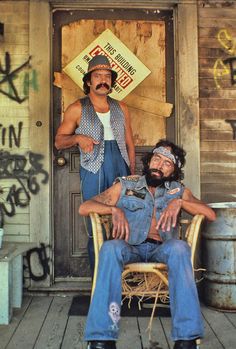 two men sitting on chairs in front of a building with graffiti written on the walls