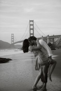 a couple kissing on the beach in front of the golden gate bridge