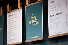 three menus are hanging on the wall in front of two wooden boards with gold lettering