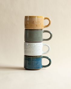 three coffee mugs stacked on top of each other in different colors and shapes,